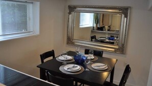 A dining area with a table set for four, a large mirror above the table, and a window with blinds. - Cozy 1 bedroom apartment, near Seattle & Airport. (Normandy Park)