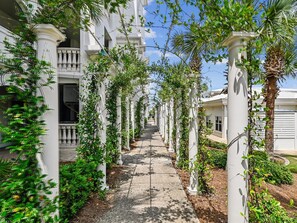A pathway flanked by white columns with greenery, leading to a building with a balcony. - Adagio #402D | Gulfside Luxury, 2 Bikes + Amenities (Santa Rosa Beach)