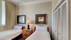 A hotel room with two single beds, a nightstand with a lamp, a ceiling fan, and a large window with curtains.