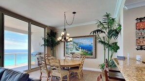 A dining area with a round table and chairs, a chandelier, and a painting of a coastal scene.