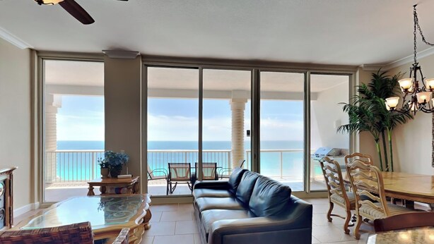 A spacious living area with a leather sofa, dining table, and chairs, overlooking a balcony with a view of the ocean.