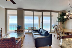 A spacious living area with a leather sofa, dining table, and chairs, overlooking a balcony with a view of the ocean. - Beach Club 1804C | Indoor/Outdoor Pool + Views! (Pensacola Beach)