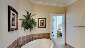 A bathroom with a large bathtub, a potted plant, and framed pictures on the wall.