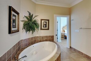 Un baño con una bañera grande, una planta en maceta y cuadros en la pared.