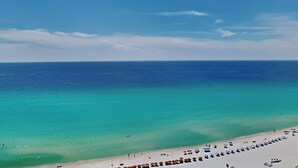 A beach with clear turquoise water and a sandy shore. There are rows of beach umbrellas and lounge chairs.