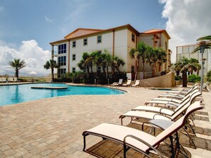 A hotel with a pool area, lounge chairs, and palm trees.