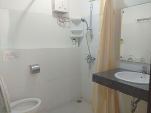 Et lille badeværelse med toilet, vask, brusebad og spejl.