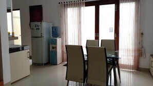 A compact living space with a kitchenette, a dining area with a table and chairs, and a large window with curtains. - Omah Dixy Family Homestay by FH Stay (Baturetno)