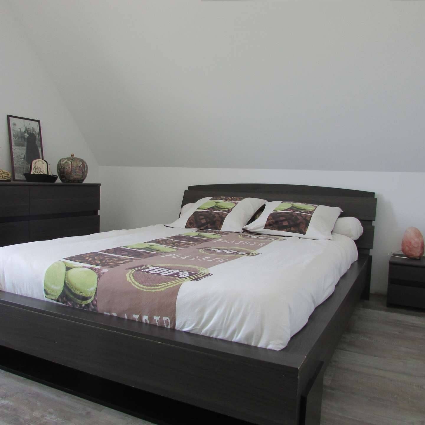 Un dormitorio con una cama de madera oscura, ropa de cama blanca y una almohada decorativa con motivos de grano de café.