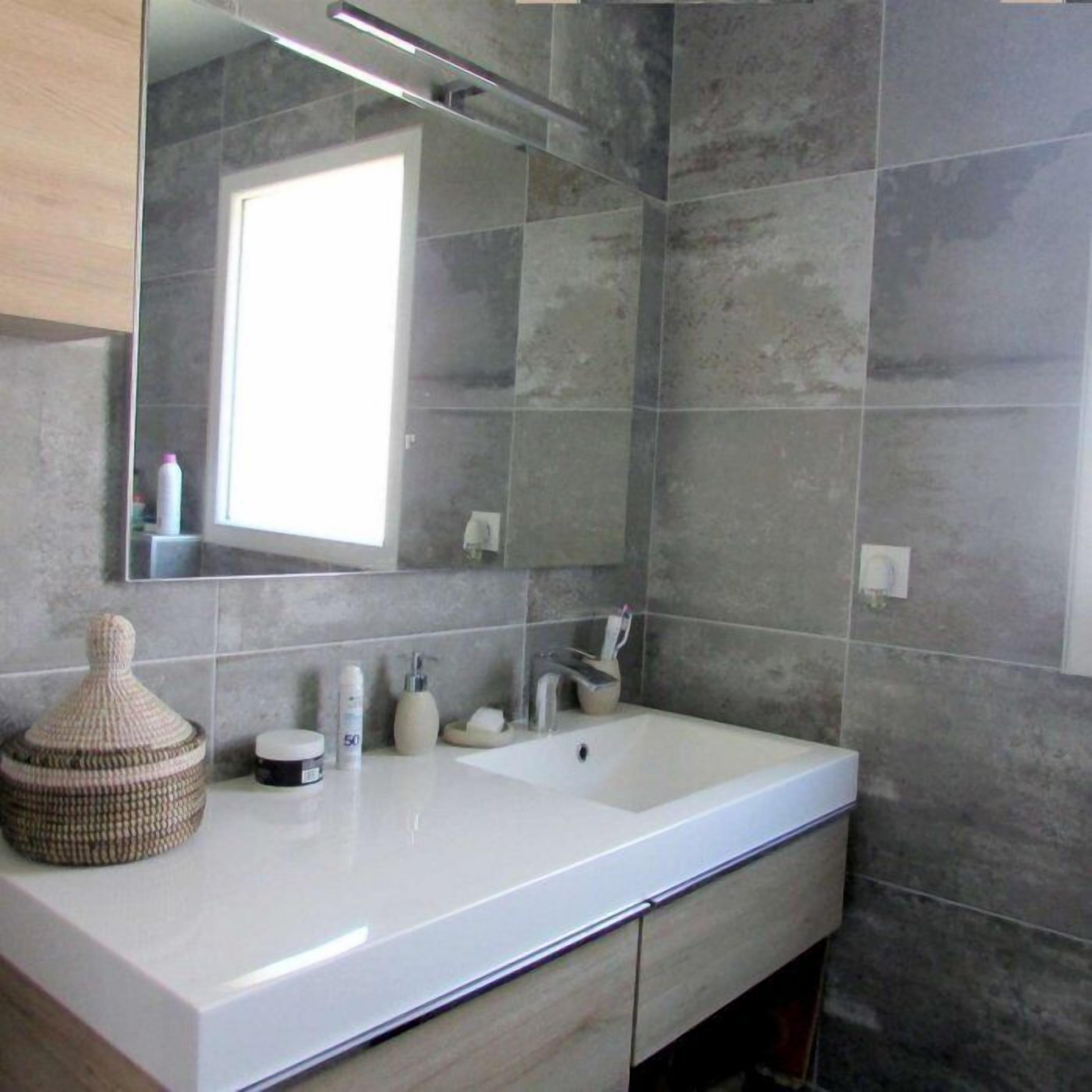 Un baño moderno con un espejo grande, un lavamanos blanco y un perchero para toallas.
