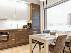 Une cuisine moderne avec des meubles en bois, un four encastré et un coin repas comprenant une table et des chaises.