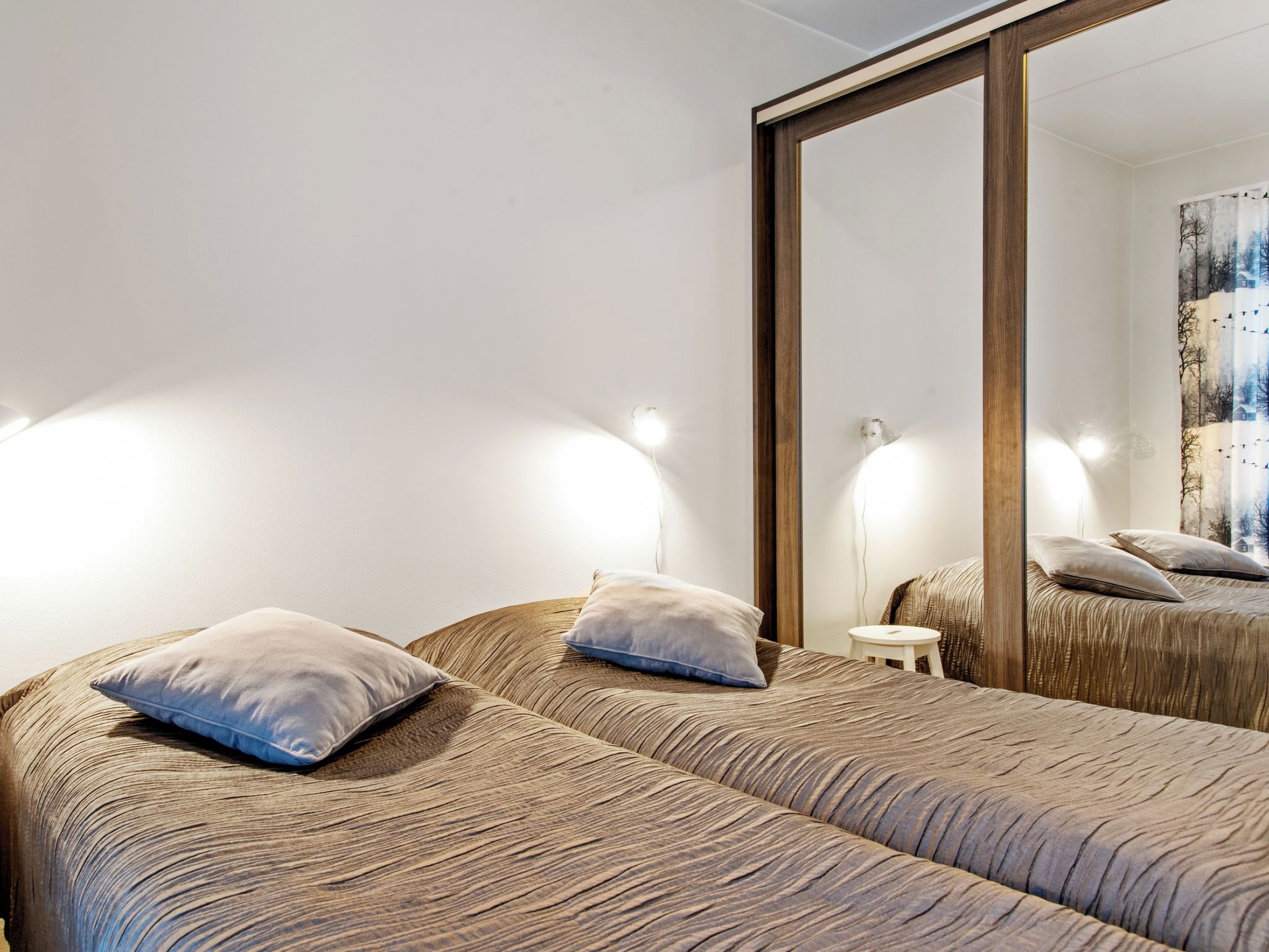 Une chambre d’hôtel avec deux lits, un grand miroir et des lampes fixées au mur.