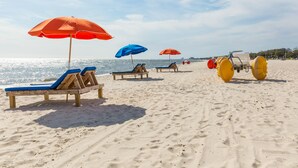 A beach with wooden lounge chairs and umbrellas, a lifeguard stand, and a clear view of the ocean.
