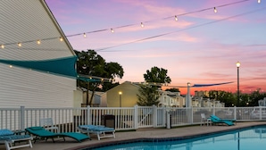 A swimming pool with lounge chairs and string lights at dusk.