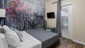 A bedroom with a bed, a wall-mounted TV, a bicycle, and a window with a curtain.