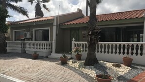 Um edifício com telhado de telhas, varanda com balaustrada branca e plantas em vasos.