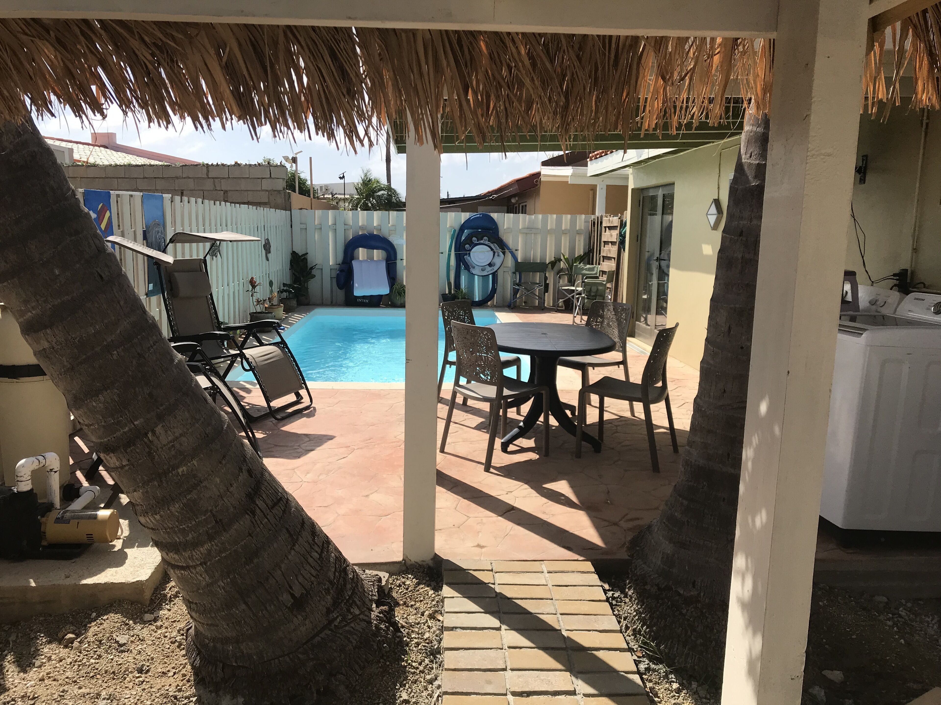 Un espacio al aire libre techado con piscina, sillas de descanso y una mesa.