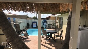 Uma área externa coberta com piscina, espreguiçadeiras e uma mesa.