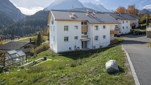 A modern residential building with a flat roof, multiple balconies, and a view of a mountain range. - Ferienwohnung STEINMANN by Interhome (Scuol)