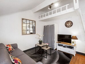 A living room with a sofa, a small table with a plant, a TV stand, and a clock on the wall.
