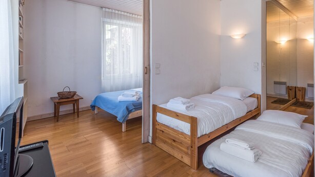 A room with two beds, a wooden floor, a window with sheer curtains, and a mirror on the wall.