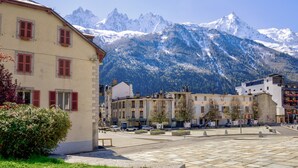 A square with buildings, a paved area, and snow-capped mountains in the background.