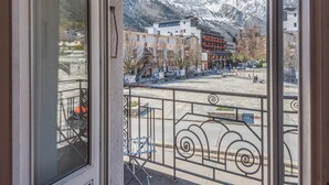 A view from a balcony with a metal railing, overlooking a parking area and buildings with a mountain backdrop.