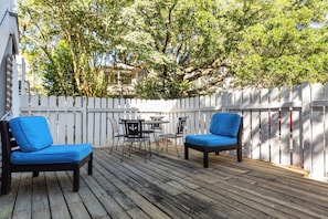 Une terrasse en bois avec deux chaises bleues et une table, entourée d’une clôture blanche en bois.