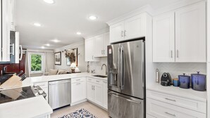 Une cuisine moderne avec des meubles blancs, des appareils en acier inoxydable et un tapis à motifs bleus.
