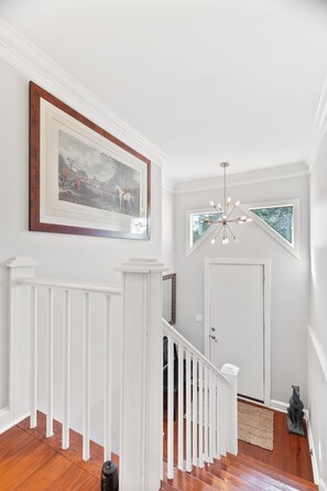 A staircase with white railings, a framed picture on the wall, a door with a window, and a hanging light fixture. - Modern and Spacious home with a fantastic, central, downtown location (Charleston)