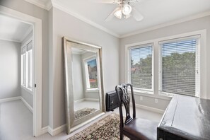 A room with a ceiling fan, a large mirror, a wooden chair, and a window with blinds.