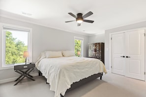 Une chambre à coucher comprenant un lit, des tables de chevet, un ventilateur de plafond et une armoire.