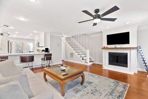 A modern living room with a sofa, coffee table, fireplace, TV, and kitchen area with bar stools. - Modern and Spacious home with a fantastic, central, downtown location (Charleston)