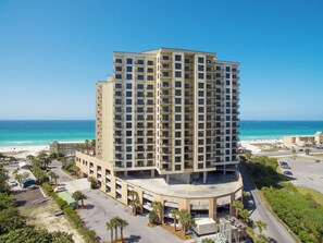 Un hotel moderno de gran altura con múltiples balcones, un aparcamiento y vistas a la playa y al océano.
