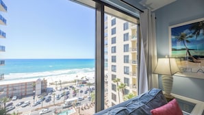 Habitación de hotel con un ventanal grande que ofrece vistas a la playa y al océano.