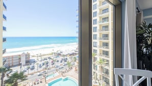 Vista desde una habitación de hotel sobre una playa con piscina y aparcamiento.