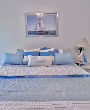 A bed with a quilted cover, a pillow with 'Ocean' embroidered, and a framed picture of a sailboat on the wall.