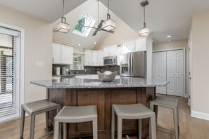 A kitchen with a central island, bar stools, a microwave, and a refrigerator.
