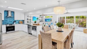 A modern kitchen with white cabinetry, a blue backsplash, and a dining area with wicker chairs. - Blue Oasis West:  Private Pool & Spa | 2 King Beds | 5-Min Walk to Beach (Holmes Beach)