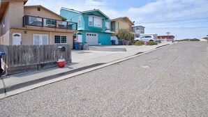 Une rue résidentielle bordée de maisons, avec une voiture blanche et une plage en arrière-plan.