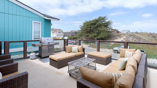 Une terrasse extérieure couverte, équipée d’un barbecue, de meubles en osier et offrant une vue sur la plage.