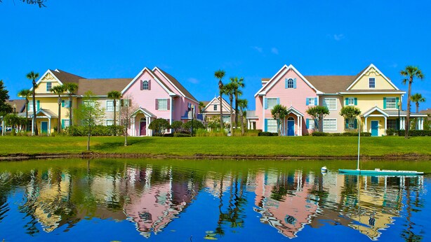 A row of pastel-colored houses with a calm water body in the foreground reflecting the buildings. - Lovely ❤️ Beach style Apt near Disney & Universal (Kissimmee)