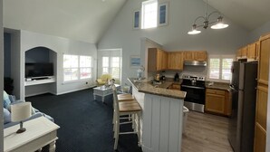 A spacious living area with a kitchen, a dining area, and a seating space with a TV and a lamp. - Lovely ❤️ Beach style Apt near Disney & Universal (Kissimmee)