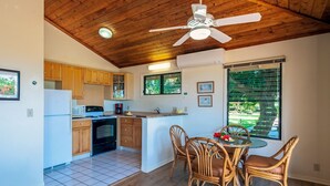 A compact kitchen with wooden cabinets, a refrigerator, an oven, and a dining area with wicker chairs and a table.
