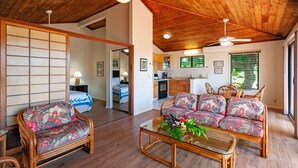 A spacious living area with a wooden ceiling, a sofa set, a dining table, and a kitchen in the background.