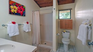 A bathroom with a shower, toilet, sink, and a painting of flowers on the wall.