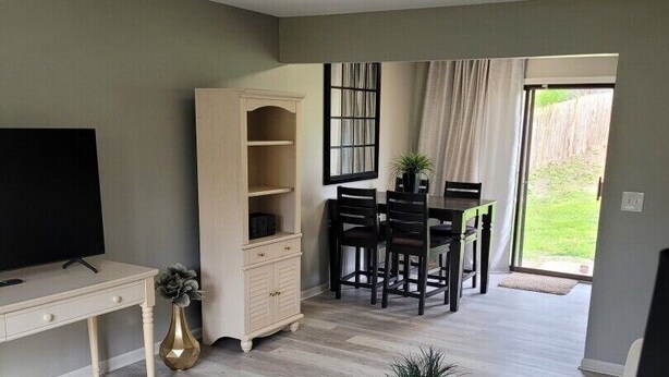 A living room with a TV, a wooden cabinet, a dining area with a table and chairs, and a large window. - Beautiful 3 Bed, 2 Bath, Sleeps 6, Full Kitchen. garage. Close to World cup! (Lee's Summit)