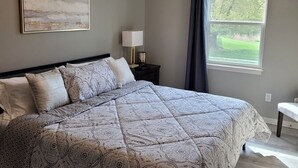 A bedroom with a large bed, a ceiling fan, a window with curtains, and a nightstand with a lamp. - Beautiful 3 Bed, 2 Bath, Sleeps 6, Full Kitchen. garage. Close to World cup! (Lee's Summit)
