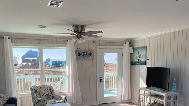 A living room with a view of the beach, a ceiling fan, a TV on a stand, and a sign that says "Sailwater". - Gulf and Bay Views in Fort Morgan! Short walk to beach. Room to park the boat! (Gulf Shores)