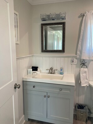 A bathroom with a white vanity, a mirror, a sink, and a towel rack.